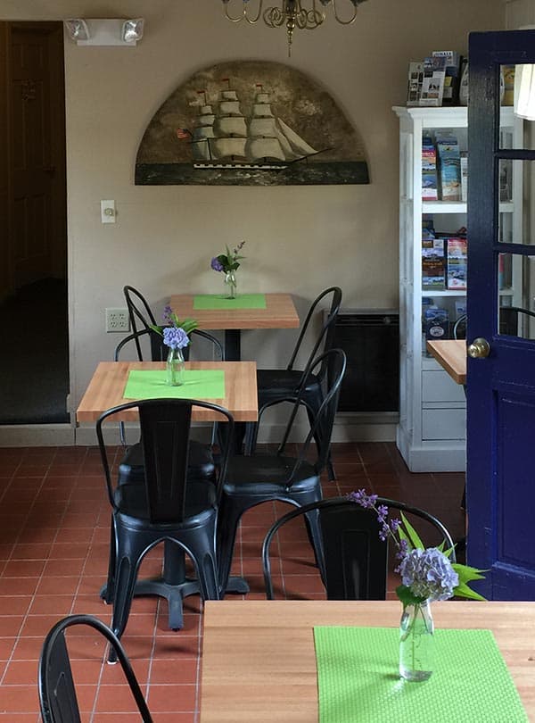 cozy room with 4 tables with flowers and green placemats, with chairs and a tile floor